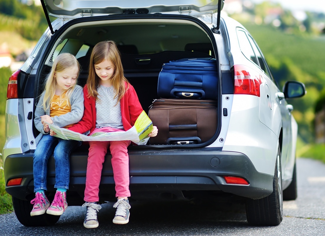 Personal Insurance - Two Little Girls Sit at the Back of a Car While Looking at a Map on a Sunny Day