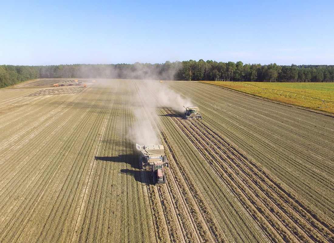 Crop Insurance - Aerial View of Harvesting Tractors Moving Through a Dry Field on a Sunny Day